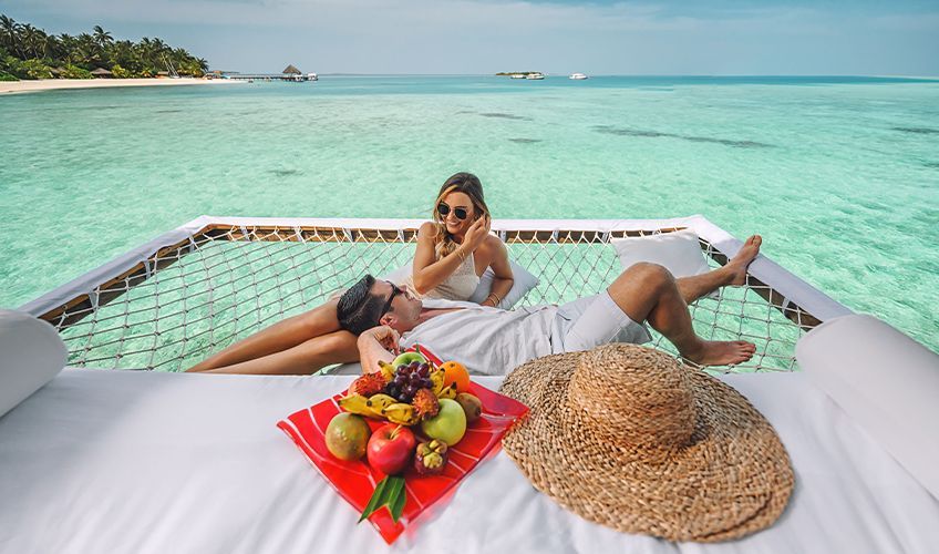 couple mangeant des fruits sur le filet d'un pilotis aux Maldives